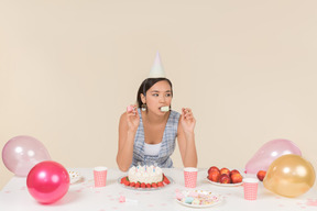 Joven mujer asiática sentada en la mesa de cumpleaños y comiendo un pastel