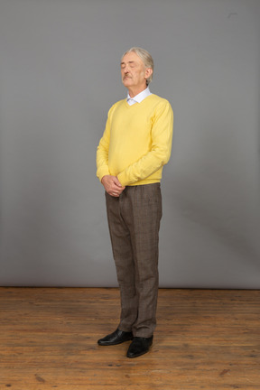 Three-quarter view of an old man in yellow pullover holding hands together with his eyes closed