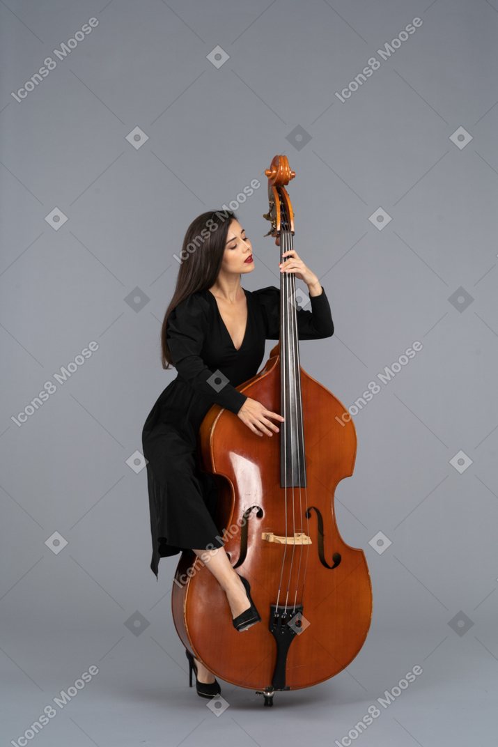 Front view of a young woman in black dress playing her double-bass putting leg on it