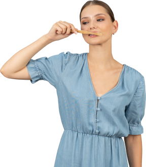 Vista frontale di una giovane donna in abito blu che si lava i denti