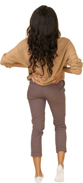 Vista posterior de una mujer joven de piel oscura poniendo las manos en las caderas y recostándose