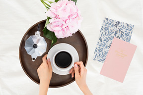 A person holding a cup of coffee next to a bouquet of flowers