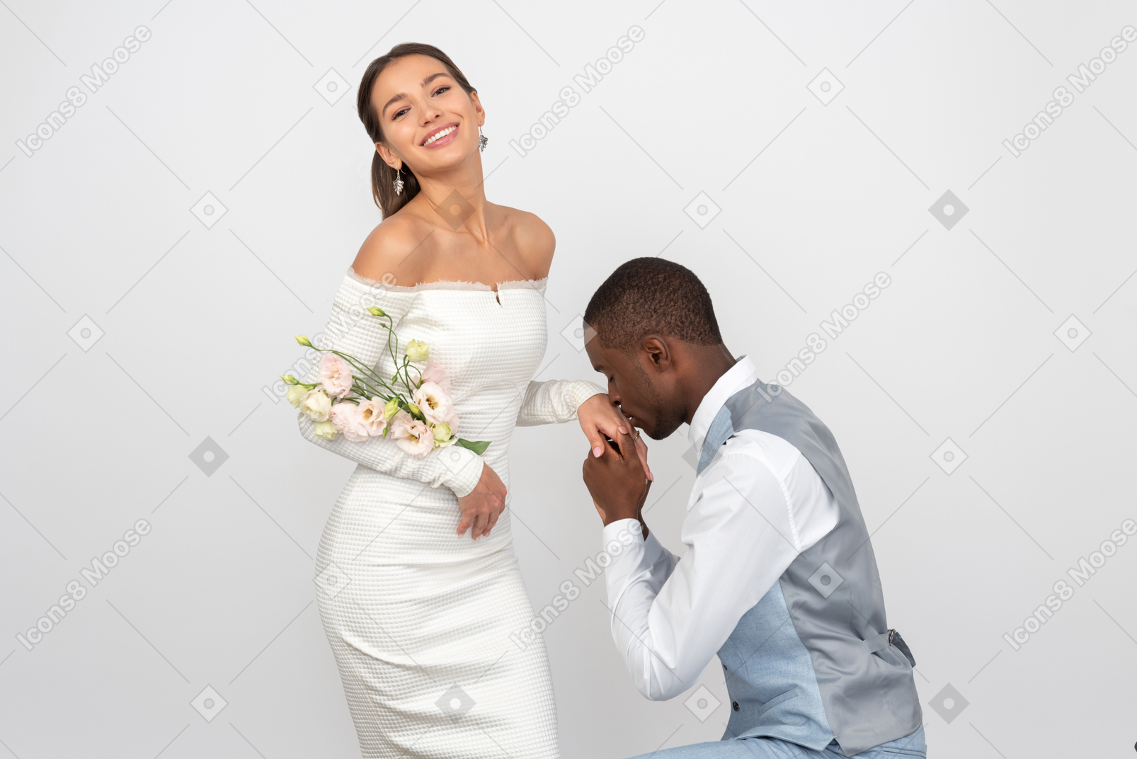 Groom kissing his bride's hand and she's holding a bouquet and smiling