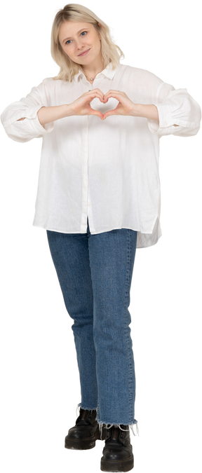 Vista frontale di una donna bionda in abiti casual che mostra un gesto del cuore e guardando da parte