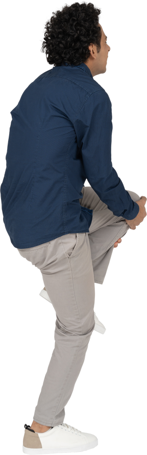 Vista laterale di un uomo in abiti casual che si tocca il ginocchio dolorante