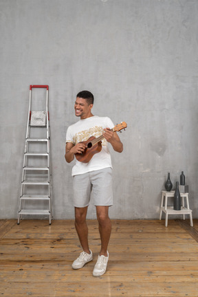 Vista di tre quarti di un uomo che suona l'ukulele e si appoggia leggermente allo schienale per la gioia