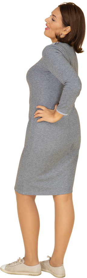 Vue latérale d'une femme en robe grise posant avec la main sur la hanche