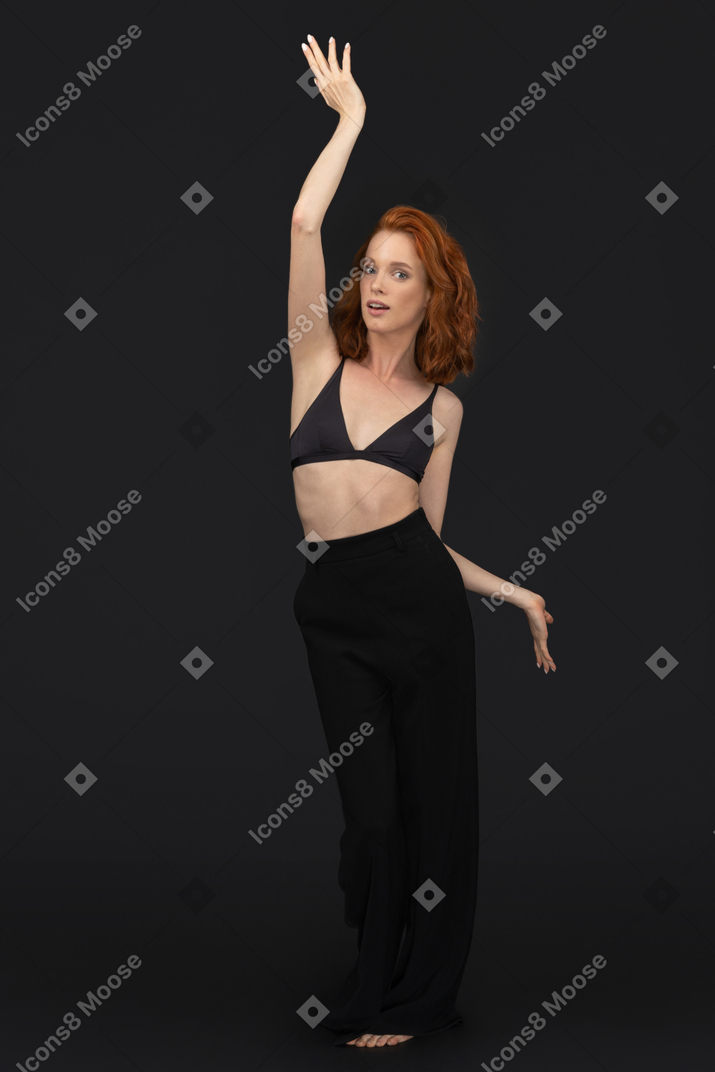 A frontal view of the cute young woman dancing on the black background and looking to the camera