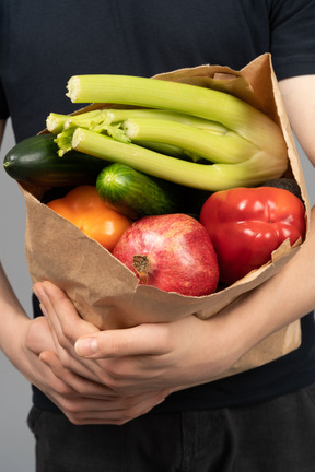 Um saco de papel cheio de frutas e legumes nas mãos do homem