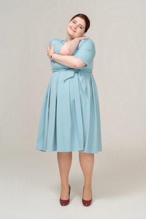 Front view of a woman in blue dress hugging herself