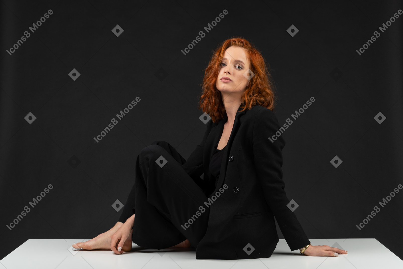 A side view of the young woman dressed in black, sitting on the table and looking to the camera