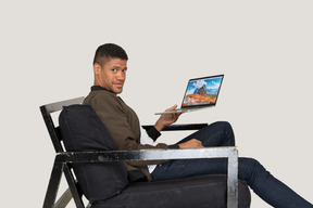 Side view of young man sitting on a sofa and holding a laptop