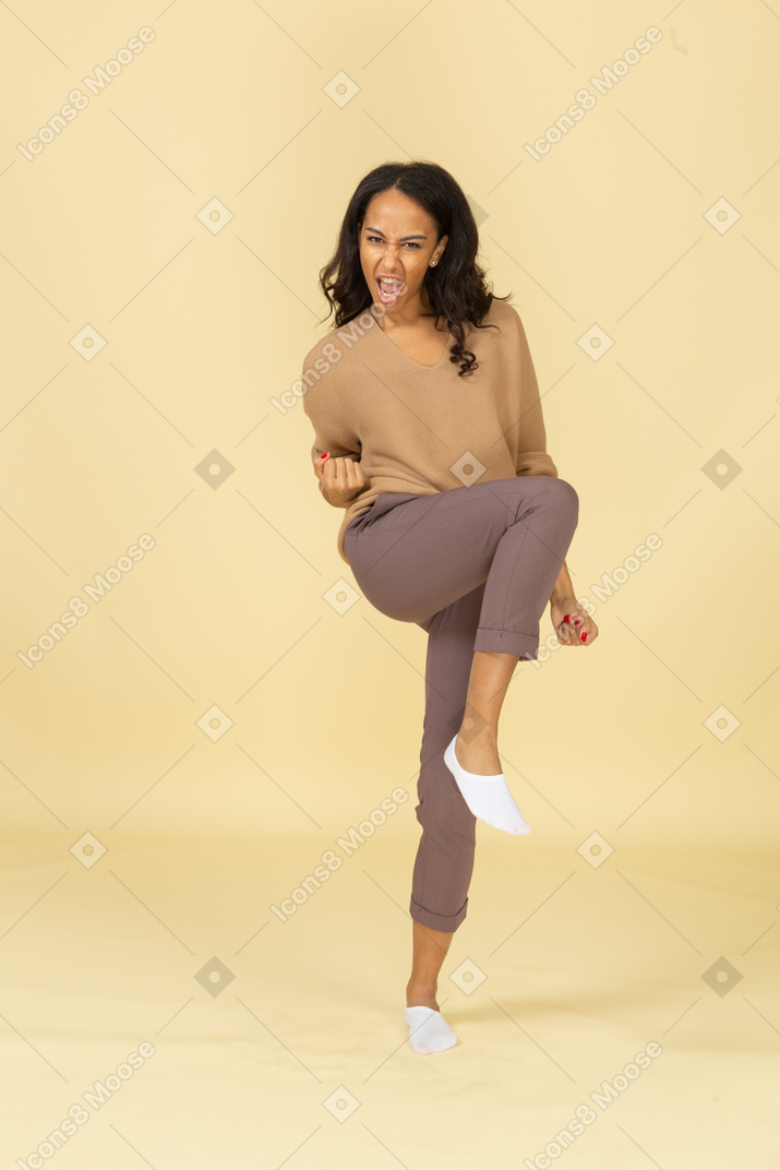 Vista frontal de uma jovem fêmea de pele escura levantando a perna e cerrando os punhos