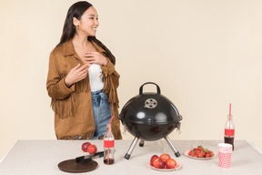 Souriante jeune fille asiatique debout près de grill sur la table