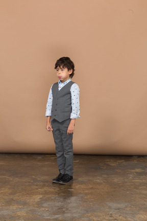 Vista frontal de un niño en traje gris hinchando las mejillas
