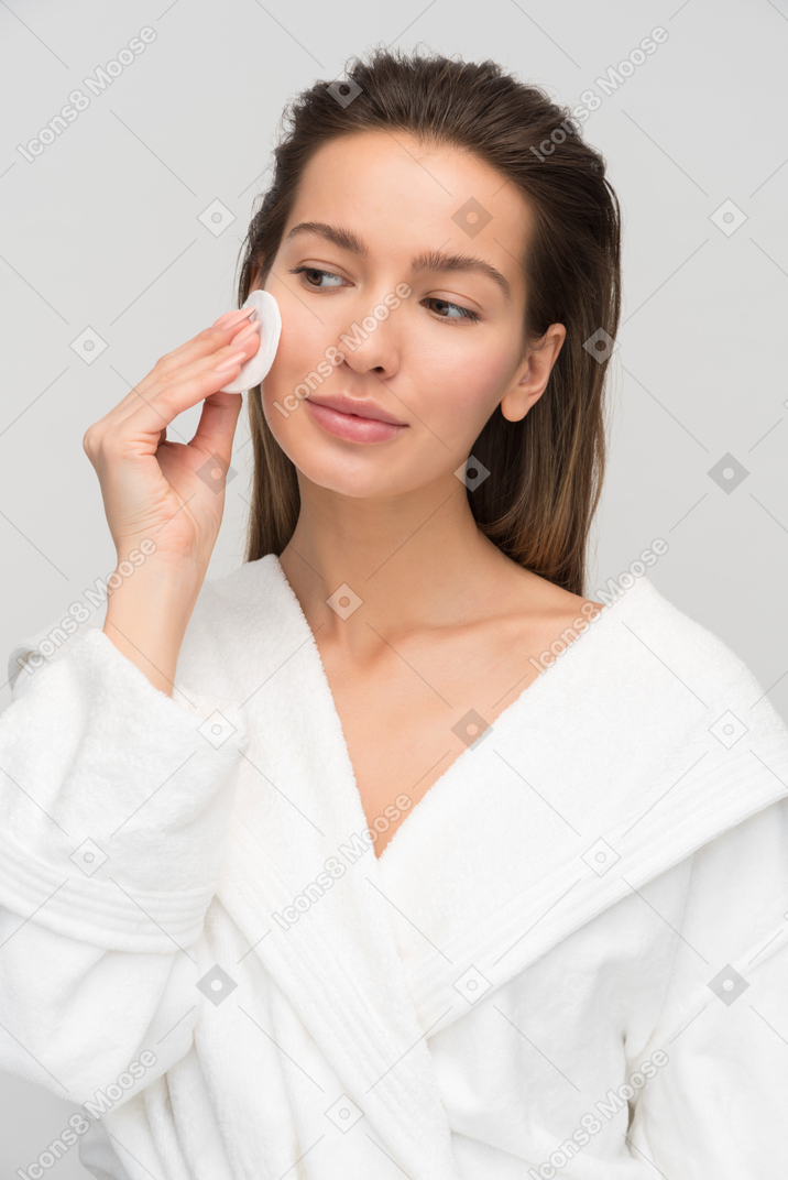 Beautiful young woman cleaning her face with cotton pad