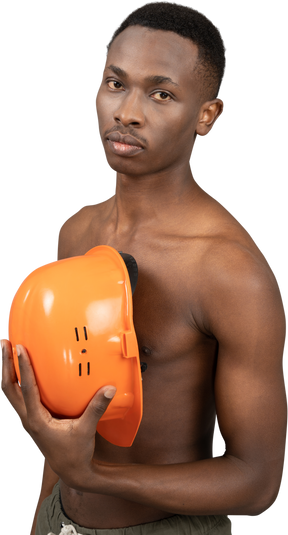Um jovem sem camisa, segurando um capacete de segurança