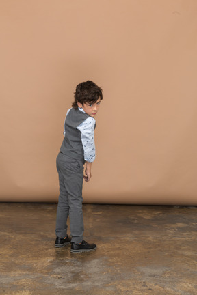 Vista trasera de un niño con traje gris mirando a la cámara