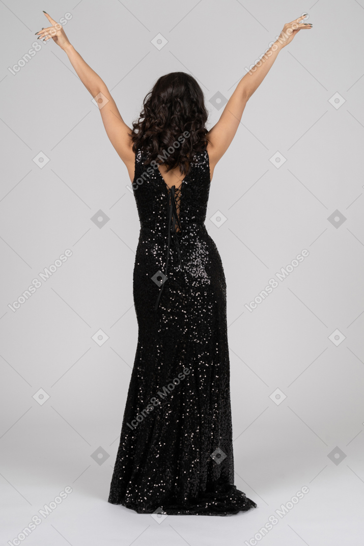 Woman in black evening dress standing back to camera with her arms in the air