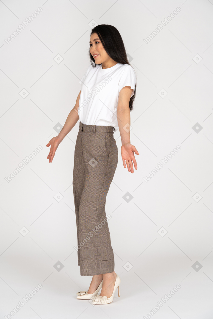 Vista di tre quarti di una giovane donna in calzoni e maglietta che allarga le mani