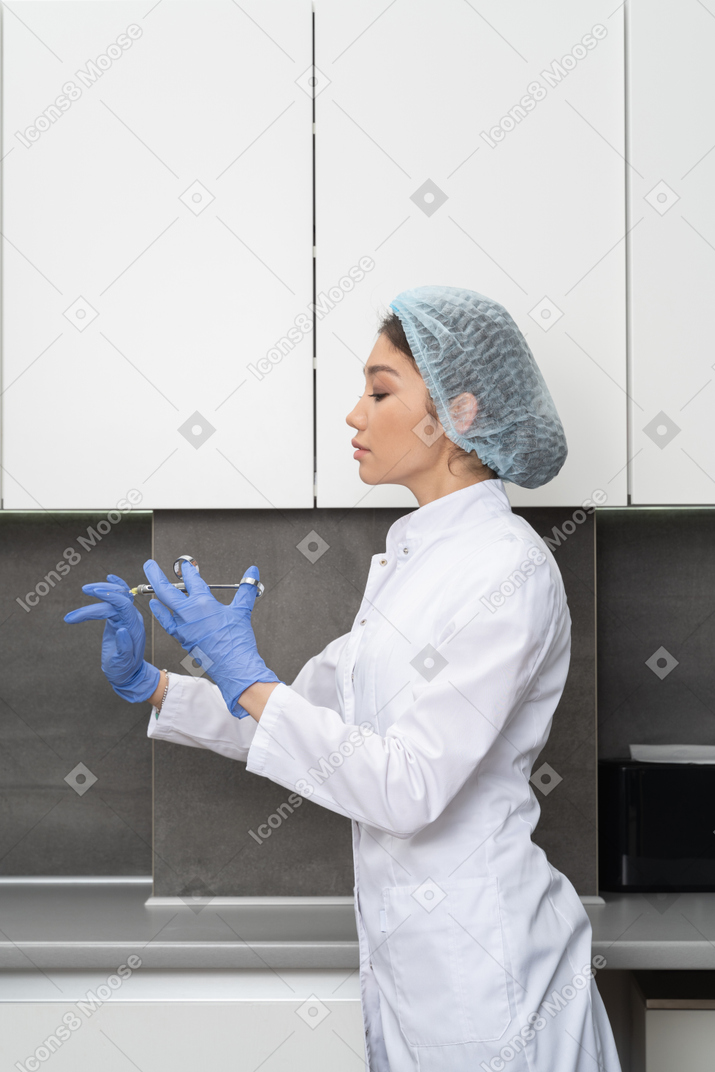 Вид сбоку женщины-врача в медицинской шляпе, проверяющей ее шприц