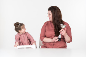 Mãe e sua filha sentada à mesa com um copo de prêmio