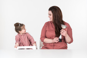 Mutter und ihre kleine tochter sitzen am tisch mit einem award cup