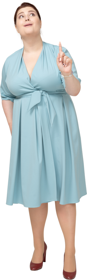 Vista frontal de una mujer en vestido azul apuntando hacia arriba con un dedo