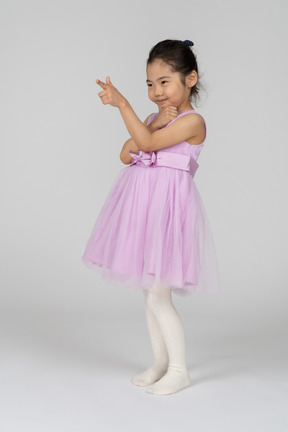 Menina asiática de vestido rosa, apontando com o dedo indicador
