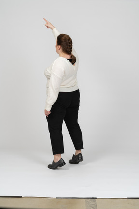 Rear view of a plump woman in casual clothes standing with raised arm