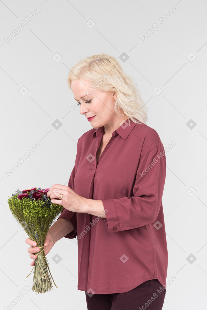 A nice-looking middle-aged blonde woman in a burgundy shirt and with a simple bouquet of flowers in her hands