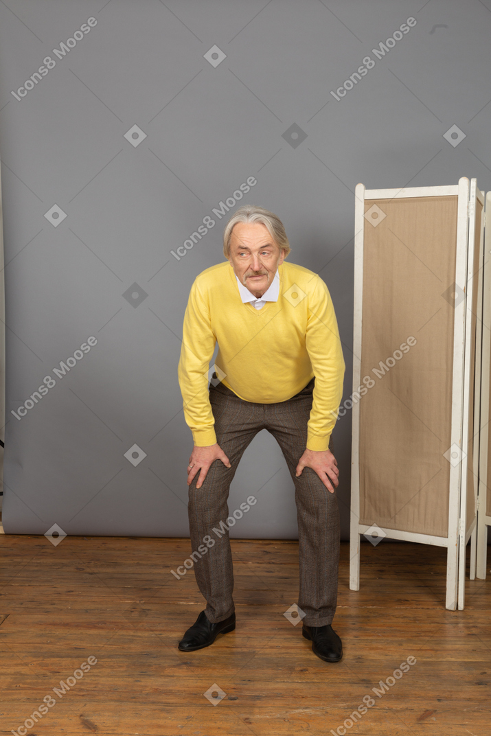 Front view of a curious old man leaning forward while putting hands on legs