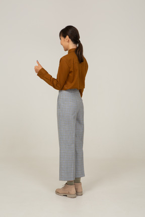 一位身着马裤和衬衫的年轻亚洲女性竖起大拇指的四分之三视图
