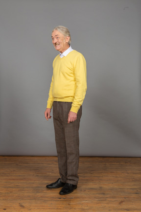 Vista de três quartos de um velho sorridente e feliz em um pulôver amarelo olhando para o lado