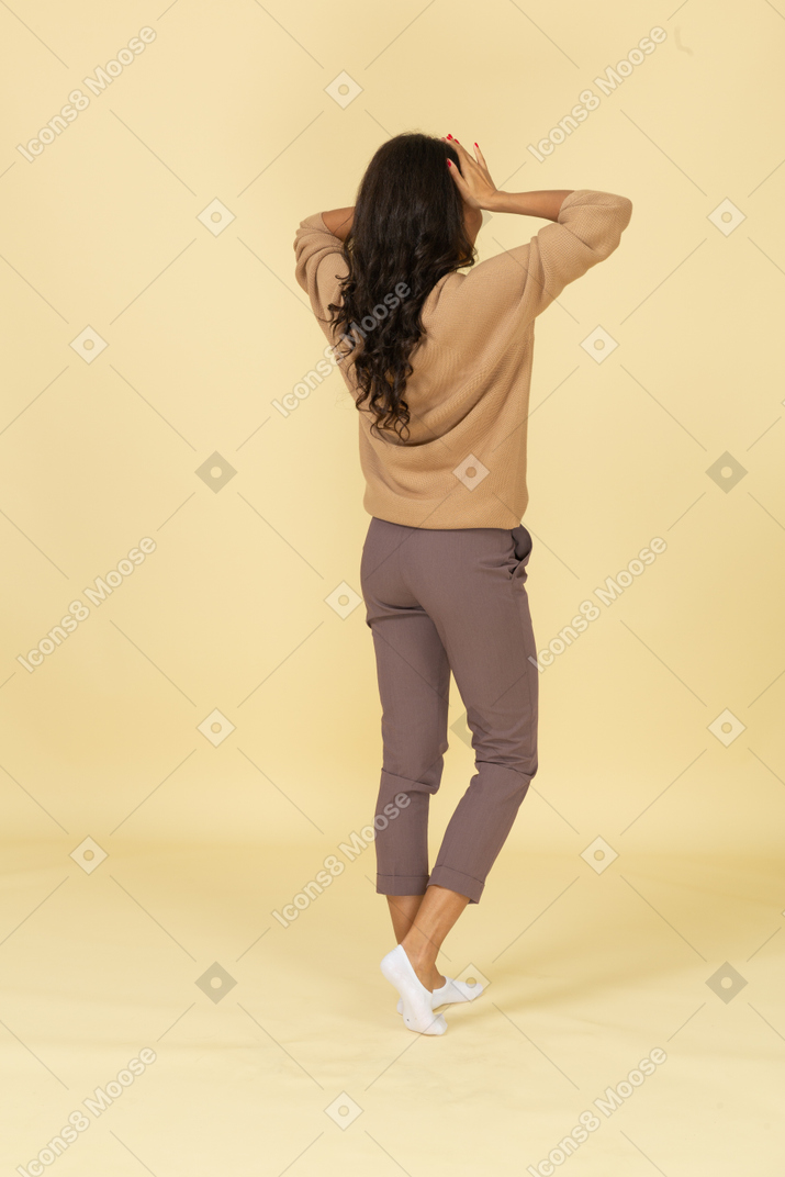 Вид сзади в три четверти темнокожей молодой женщины, касающейся ее головы