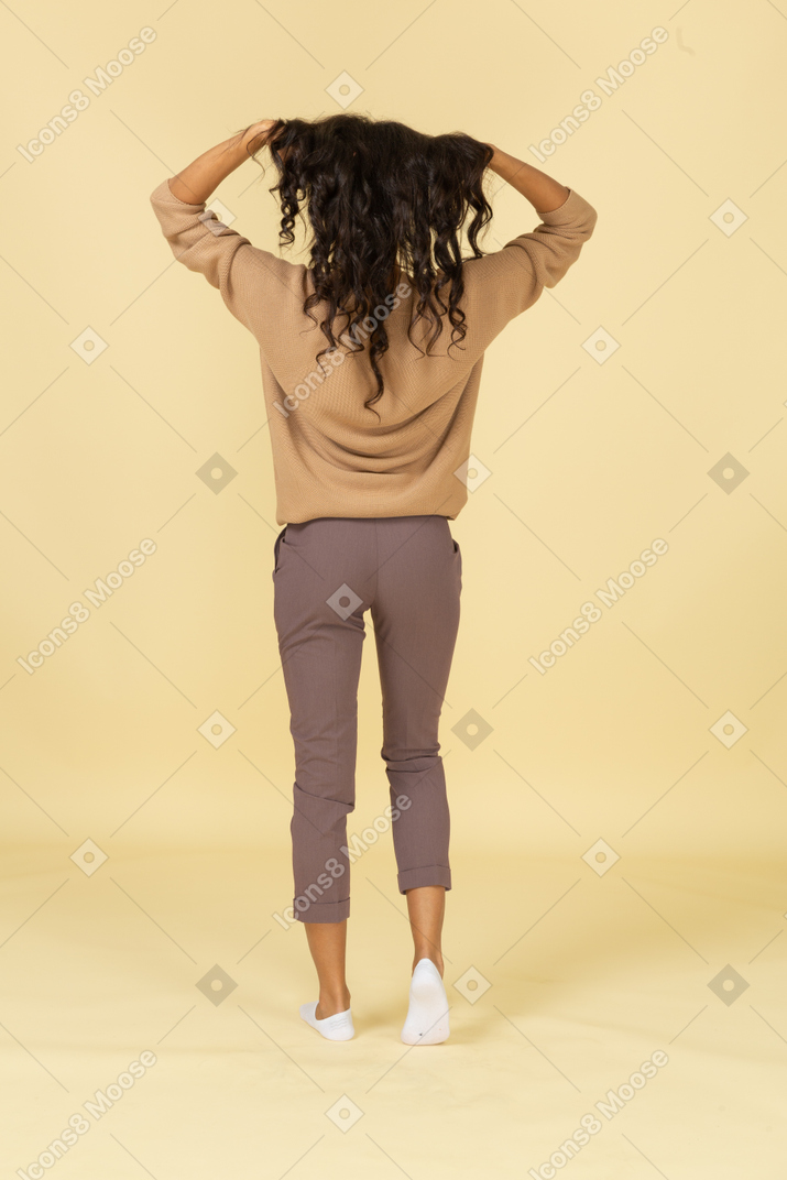 Vista posteriore di una giovane donna dalla carnagione scura che fissa i suoi capelli