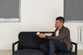 Three-quarter view of a young dreaming man sitting on a sofa with a cup of coffee