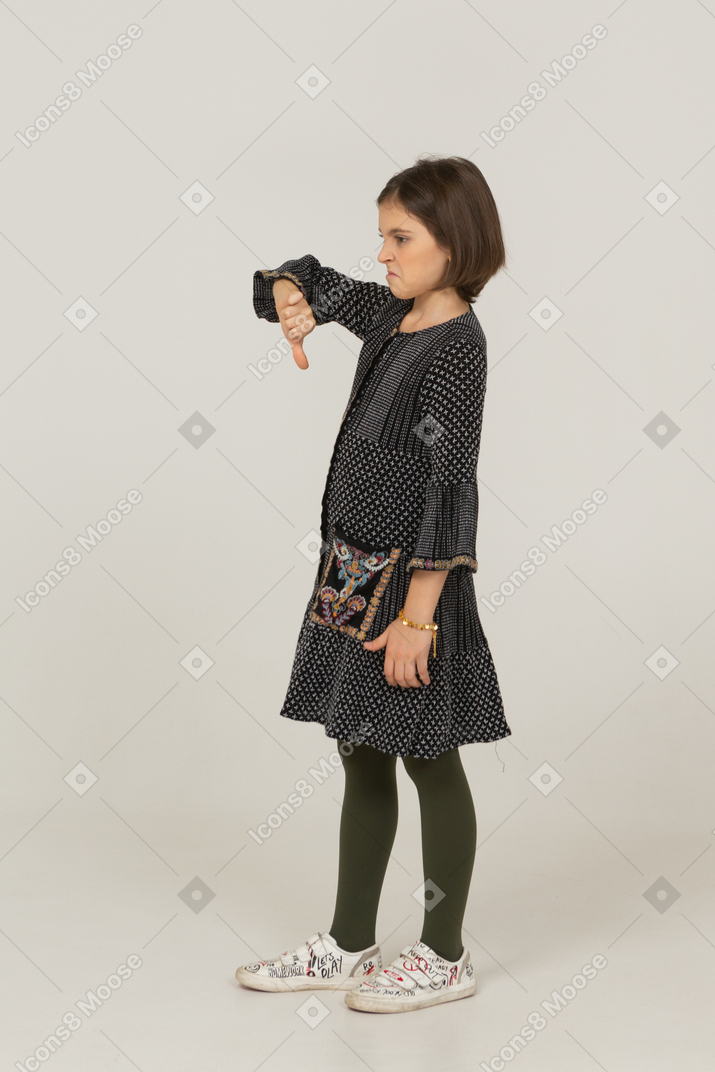 Vue latérale d'une petite fille mécontente en robe montrant le pouce vers le bas