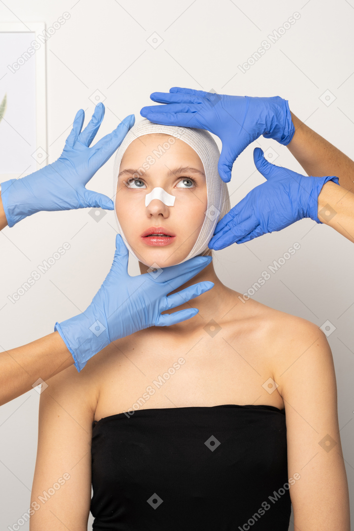 Young woman with head bandage surrounded by hands