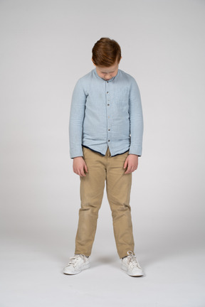 Vista frontal de um menino em roupas casuais, abaixando a cabeça