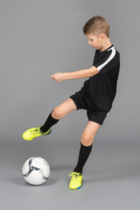 Front view of a kid boy in football uniform kicking a ball