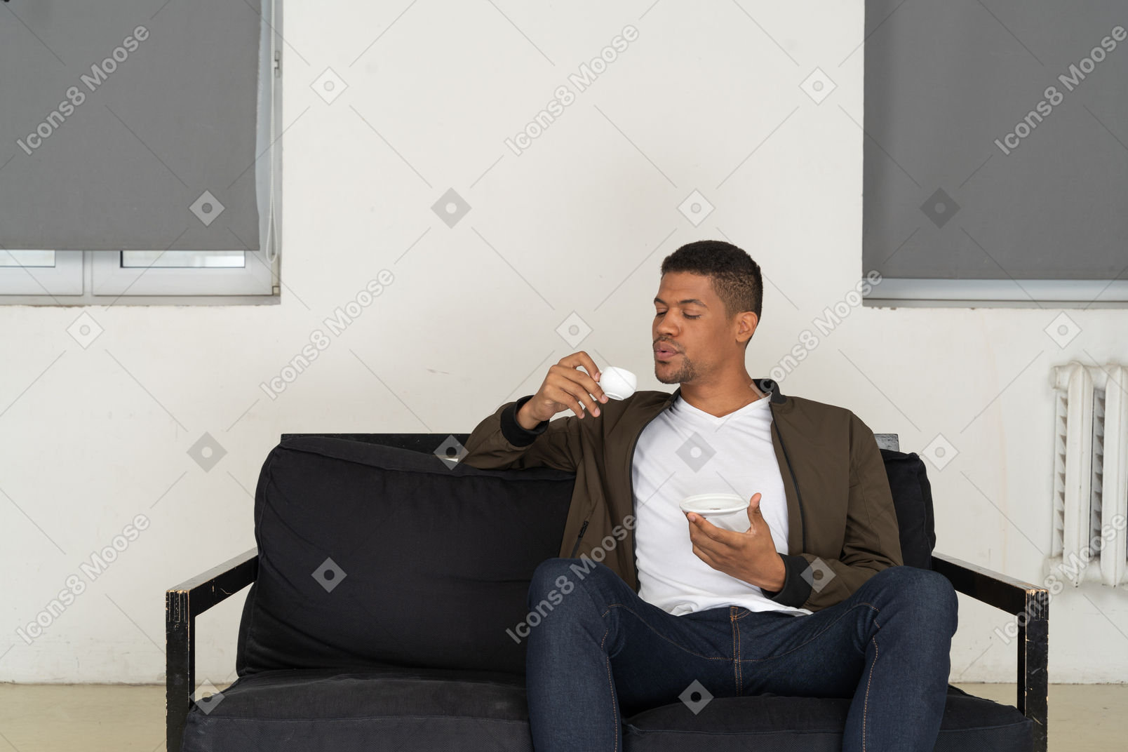 Vista frontal de un joven soñando sentado en un sofá mientras bebe café
