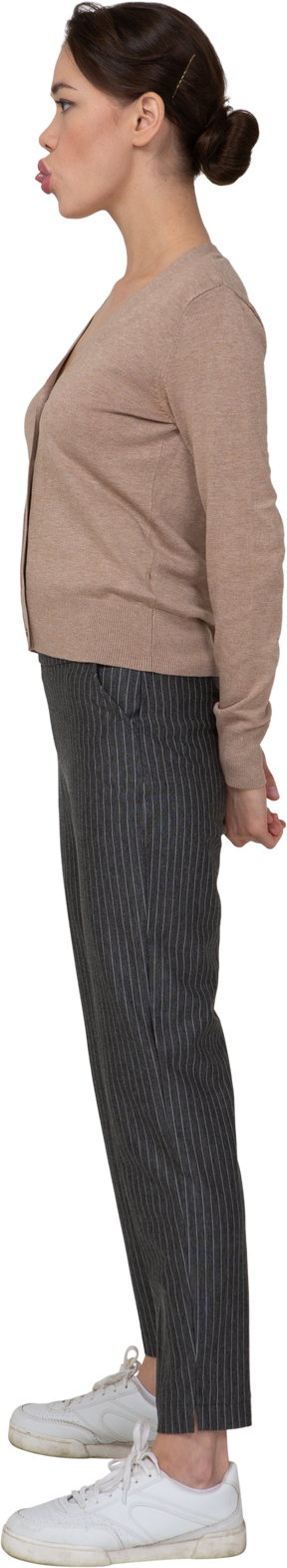 Vista laterale di una giovane donna in pullover e pantaloni che mostra la lingua