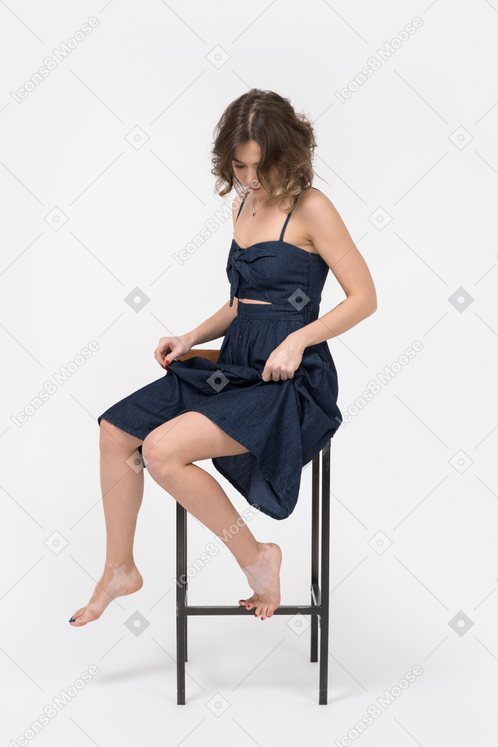 Caucasian brunette woman adjusting her dress while sitting on bar stool