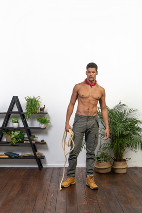 Front view of strong young man standing with a rope in his hand and looking at camera