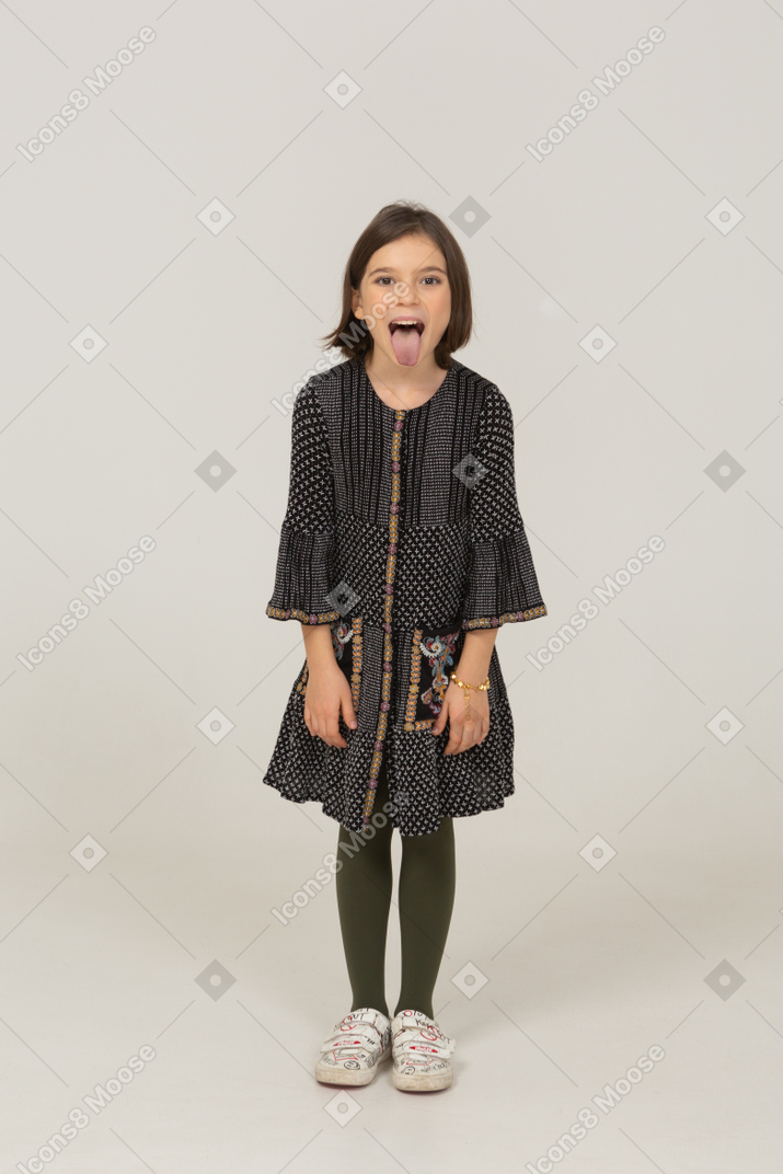 Vue de face d'une petite fille en robe se penchant en avant et montrant la langue