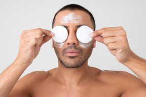 Attractive young man holding cotton pads on his eyes