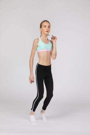Three-quarter view of a teen girl in sportswear raising hand while squatting
