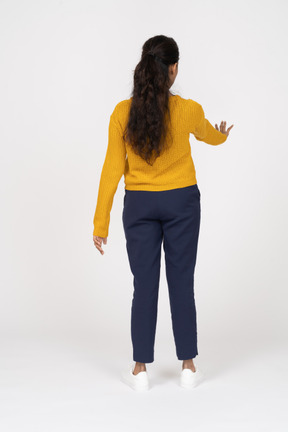 Vista posterior de una niña en ropa casual mostrando gesto de parada