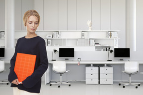 A woman standing in an office holding an orange folder